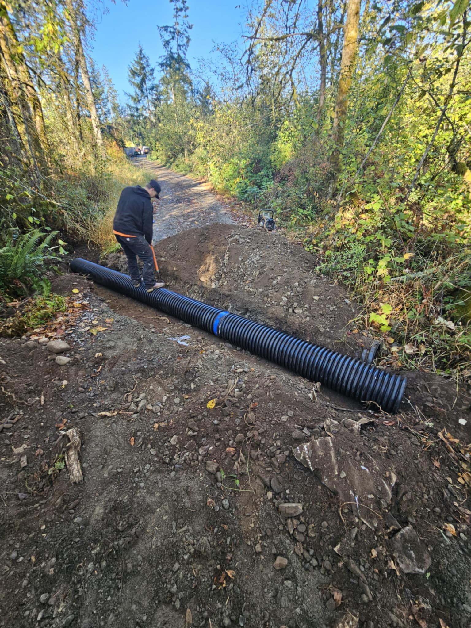 A man is standing next to a large pipe in the middle of a dirt road.