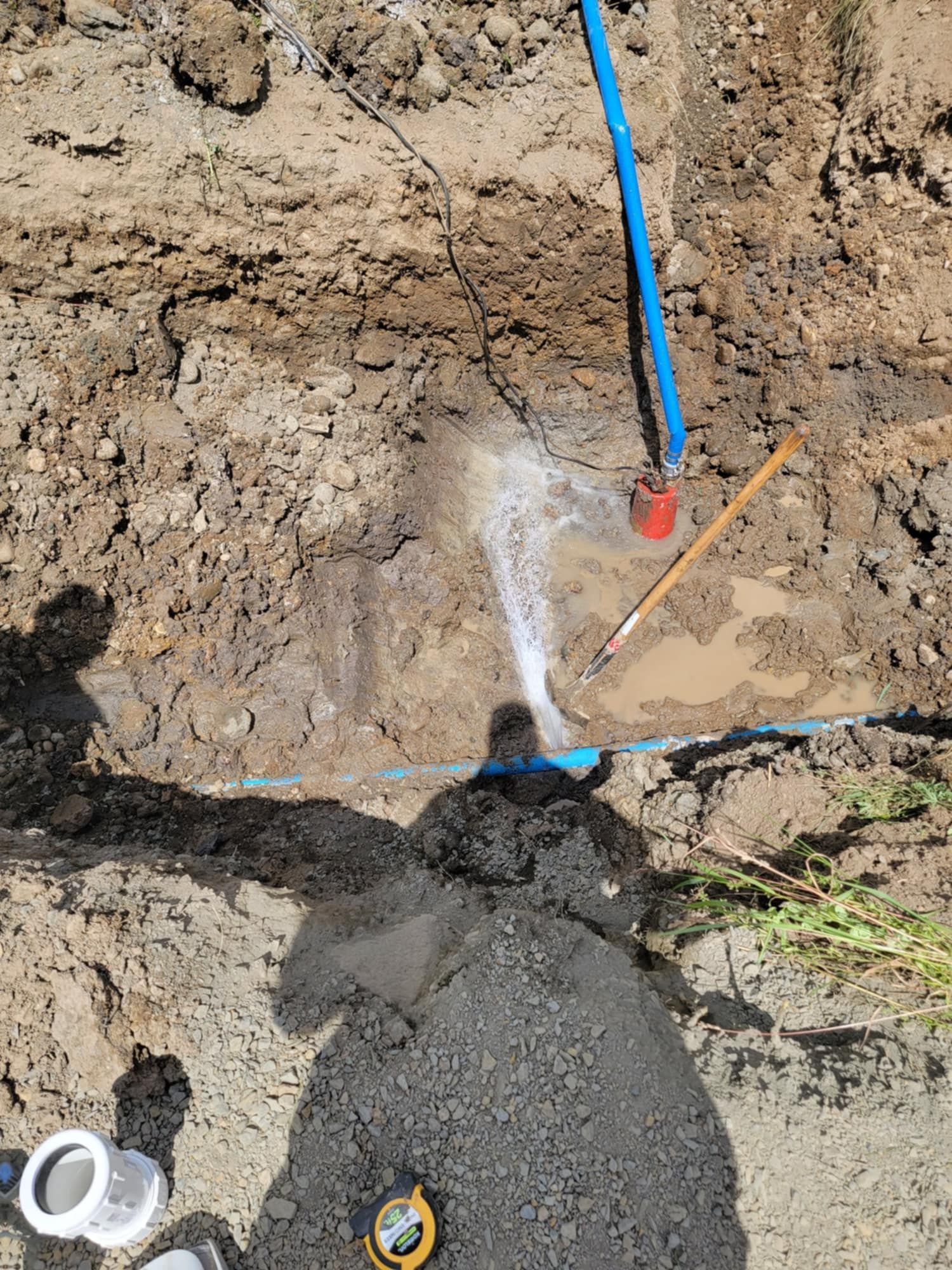 A person is standing in the dirt next to a blue pipe.