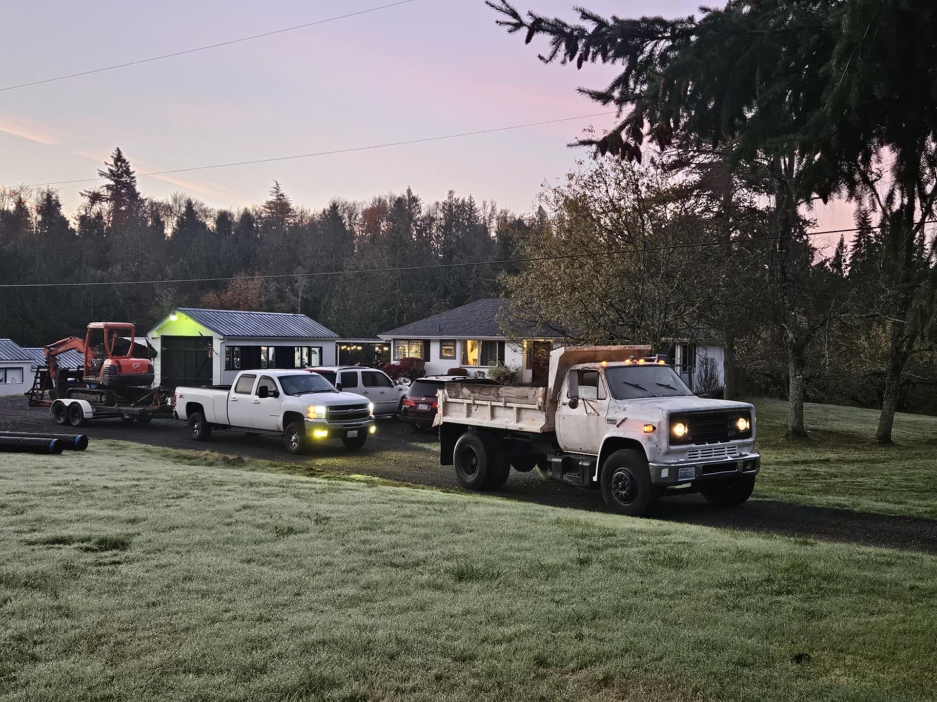 A row of trucks are parked in a grassy field in front of a house.
