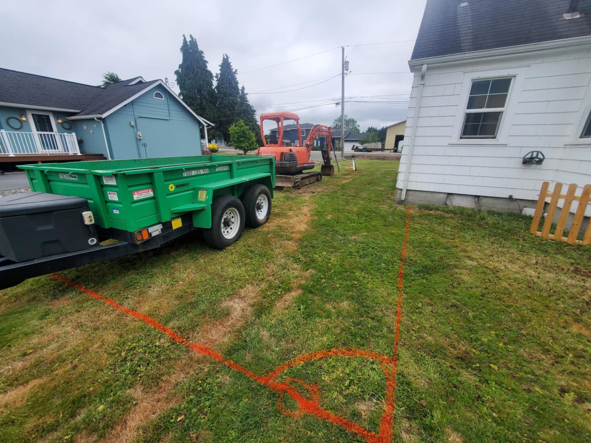 A green trailer is parked in front of a white house.