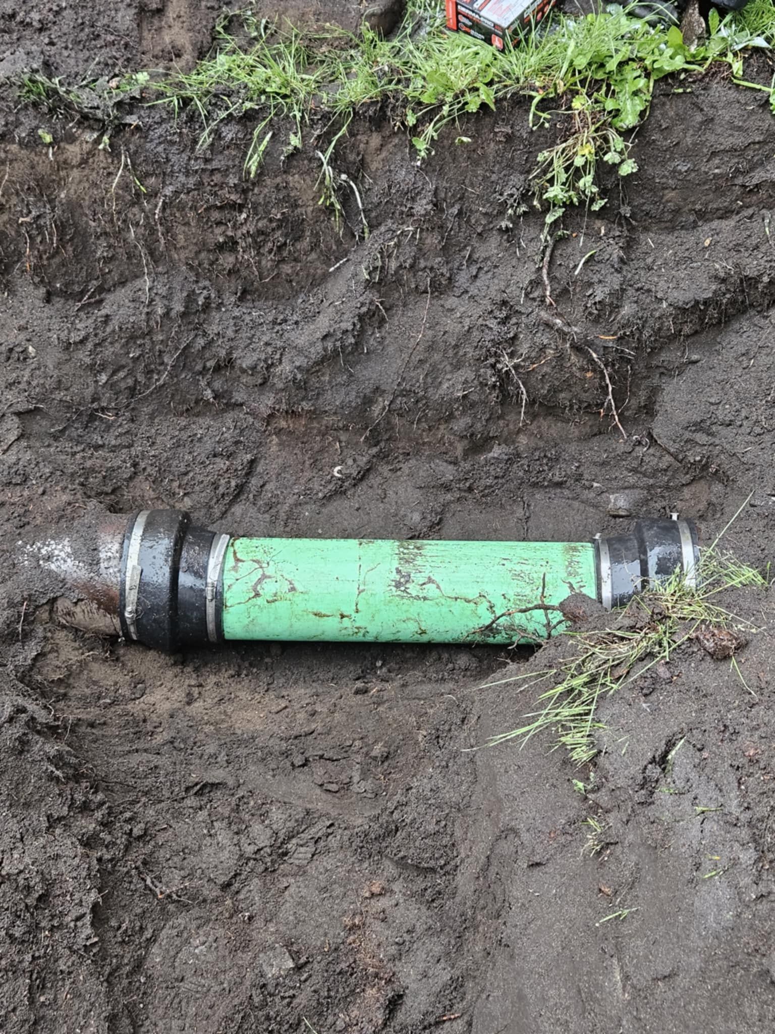 A green pipe is laying in the dirt on the ground.