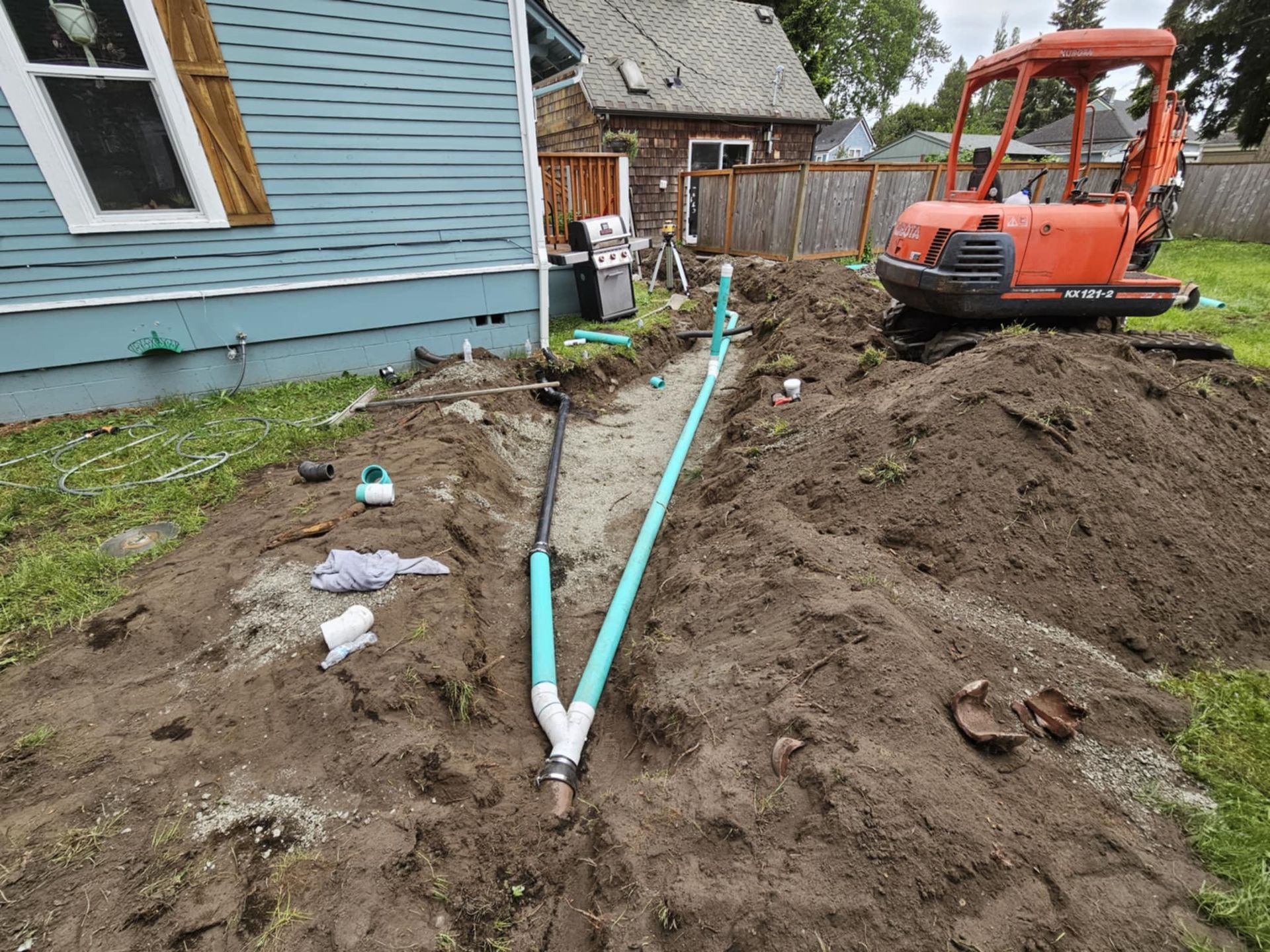 A small orange excavator is digging a hole in the dirt in front of a house.