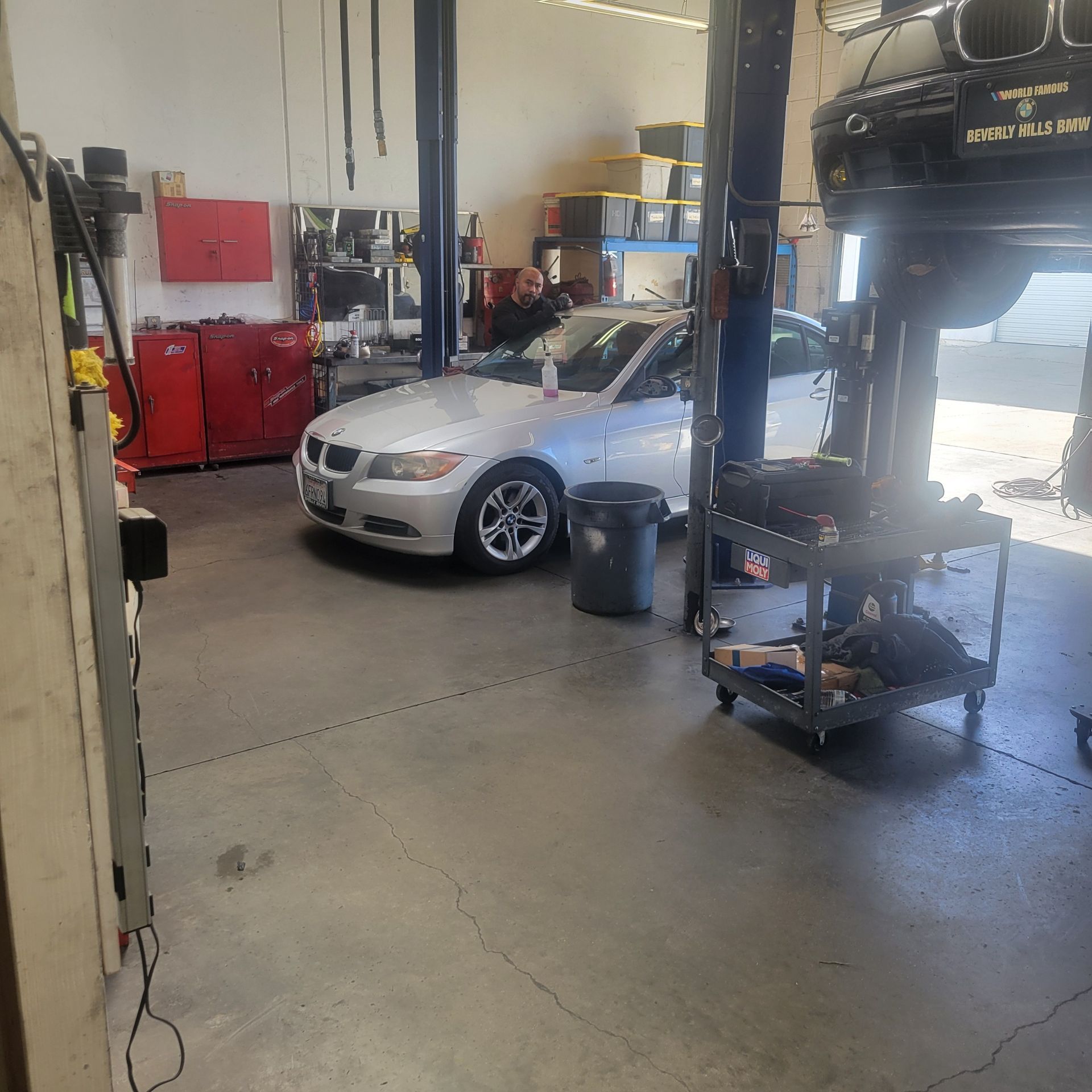 Silver sedan in an auto repair shop with a mechanic working in the background.