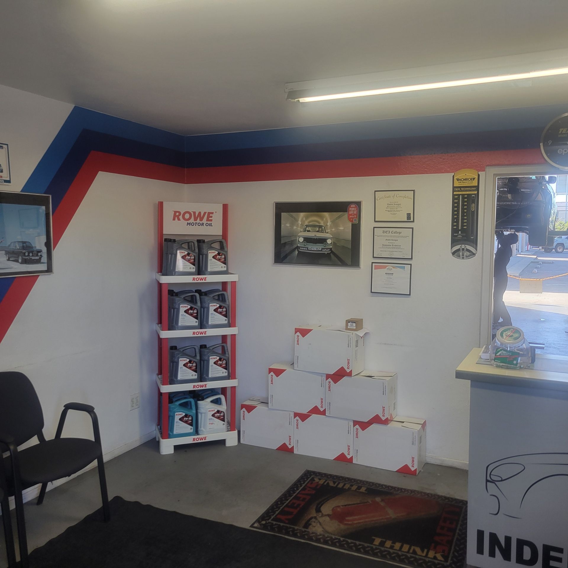 Small office corner with chairs, shelves, wall art, and a white box display under a fluorescent light.