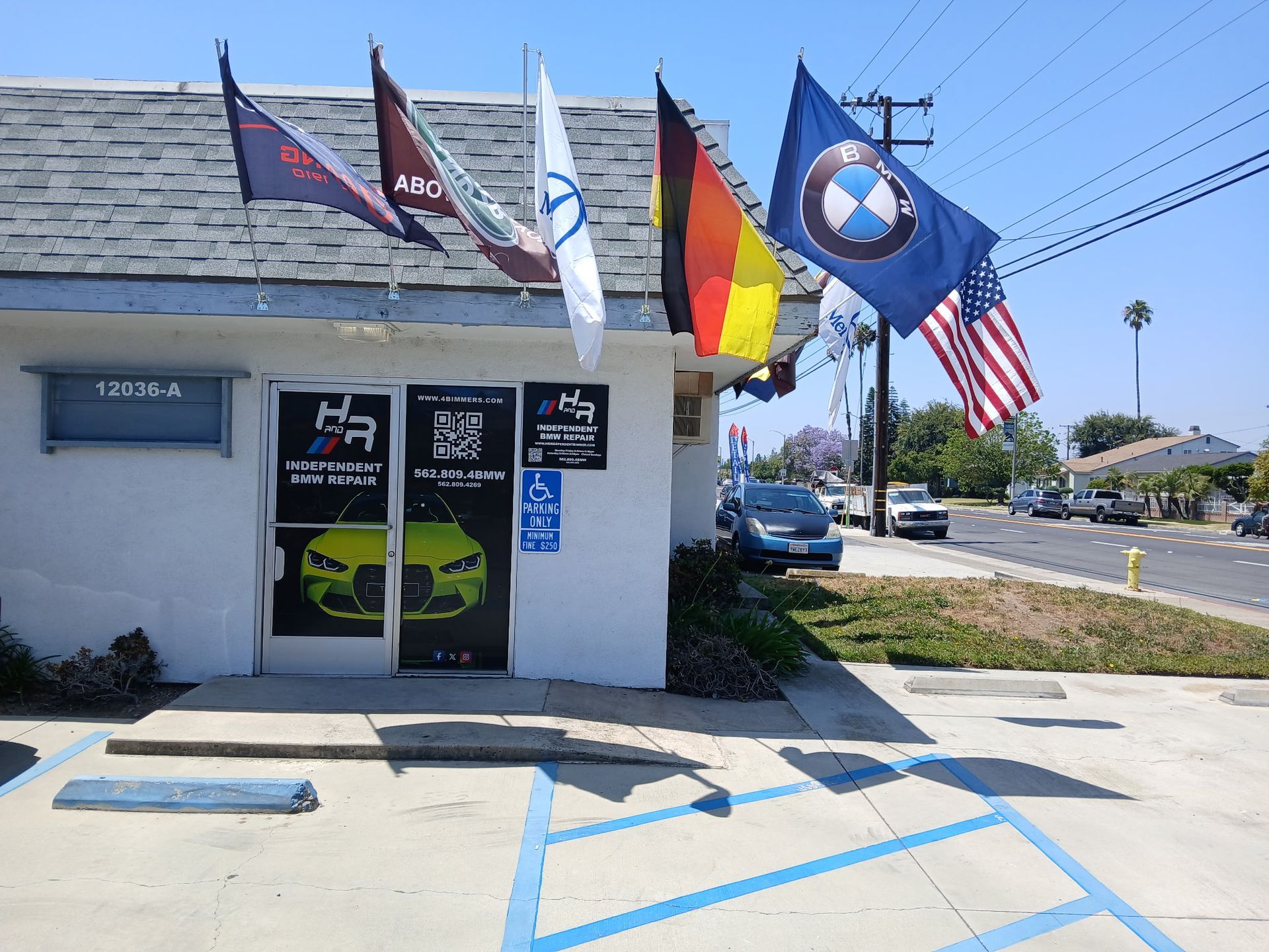 Small auto shop with flags and blue handicap parking spaces outside on a sunny street.