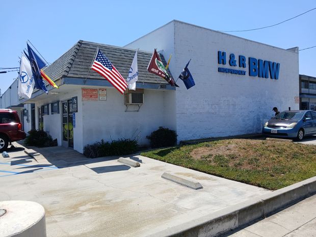 Exterior of H&R Block office with American flags and parked cars on a sunny day