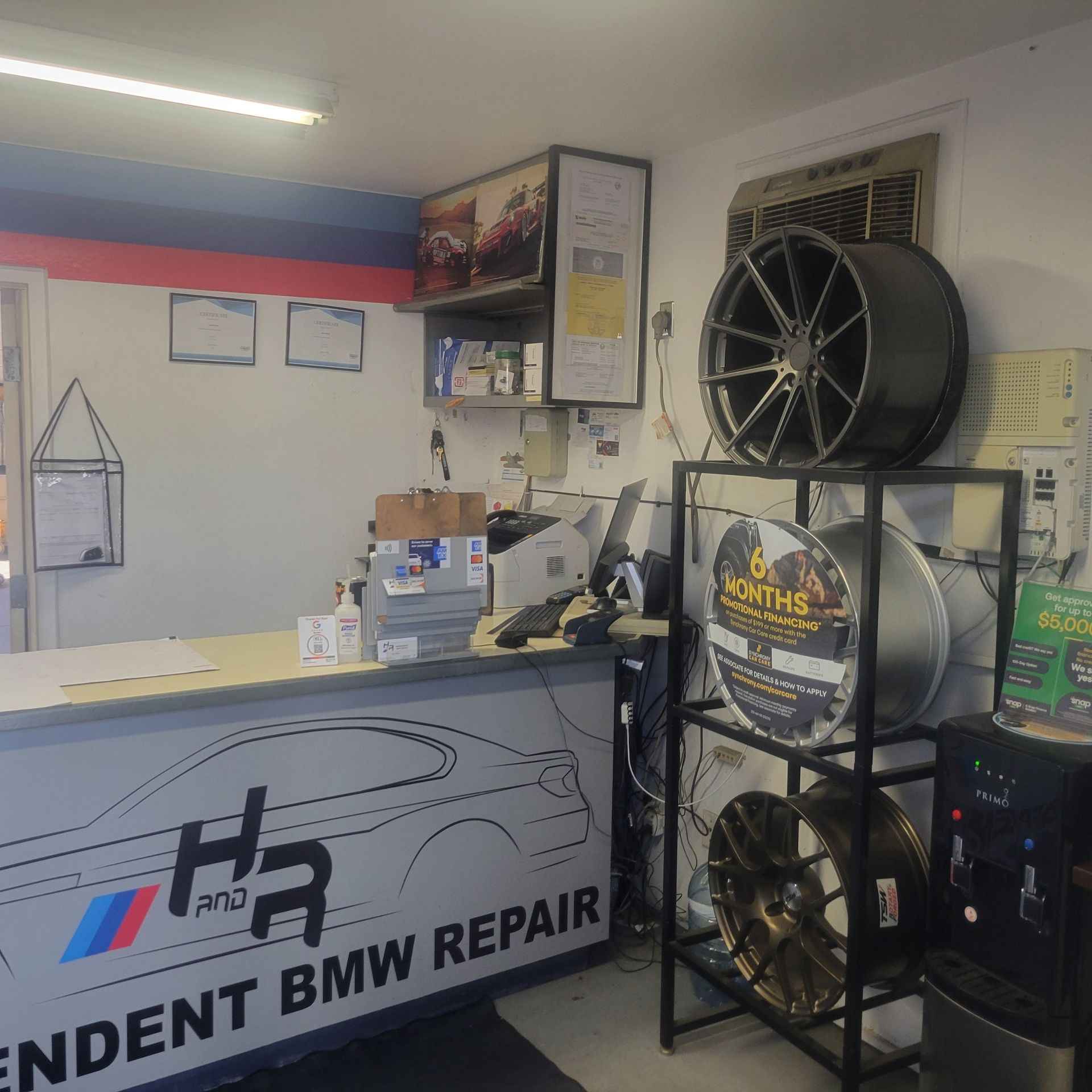 Interior of a BMW repair shop with a front desk, signage, and large industrial fans.