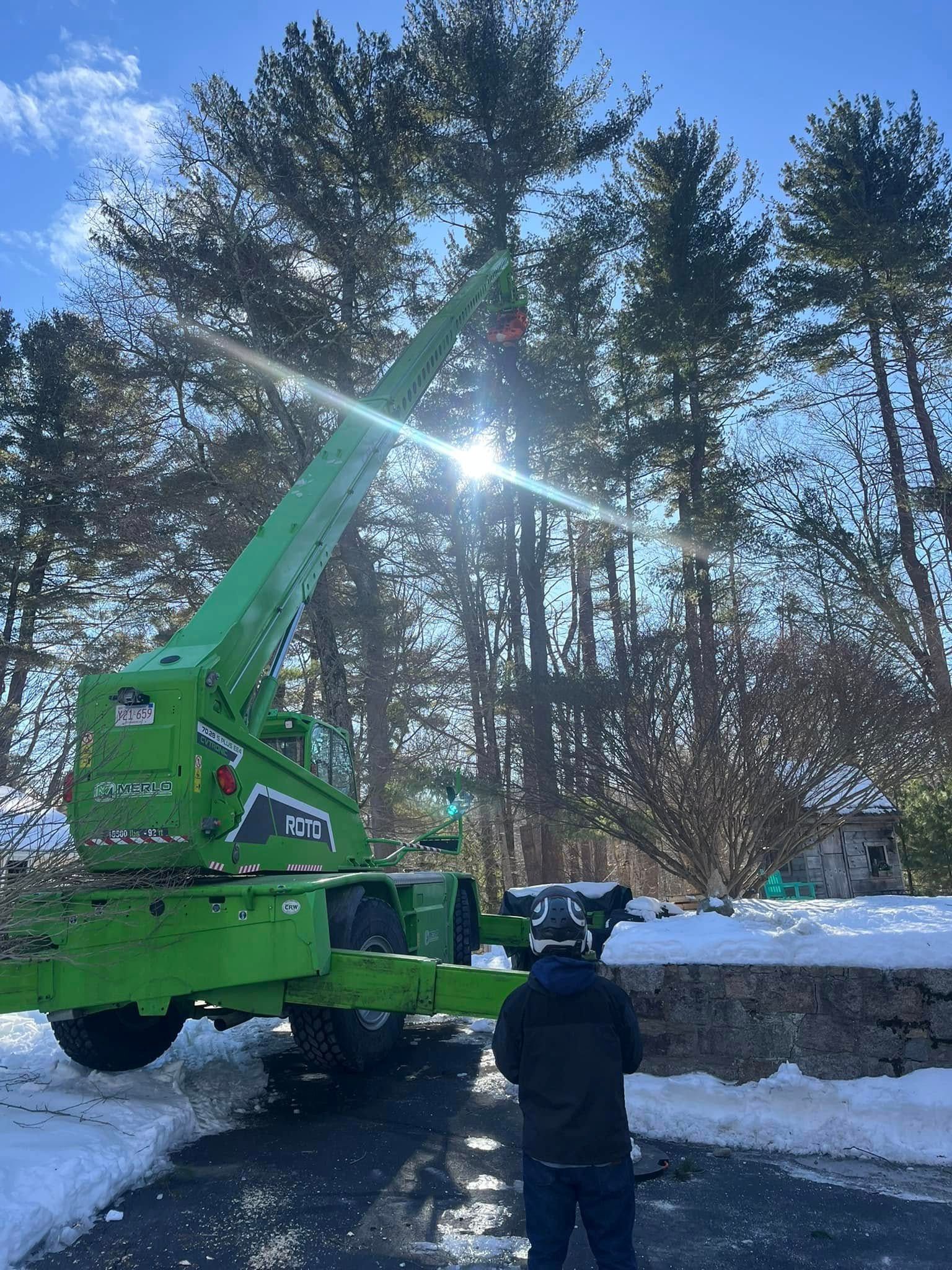 A man is standing in front of a green crane in the snow.