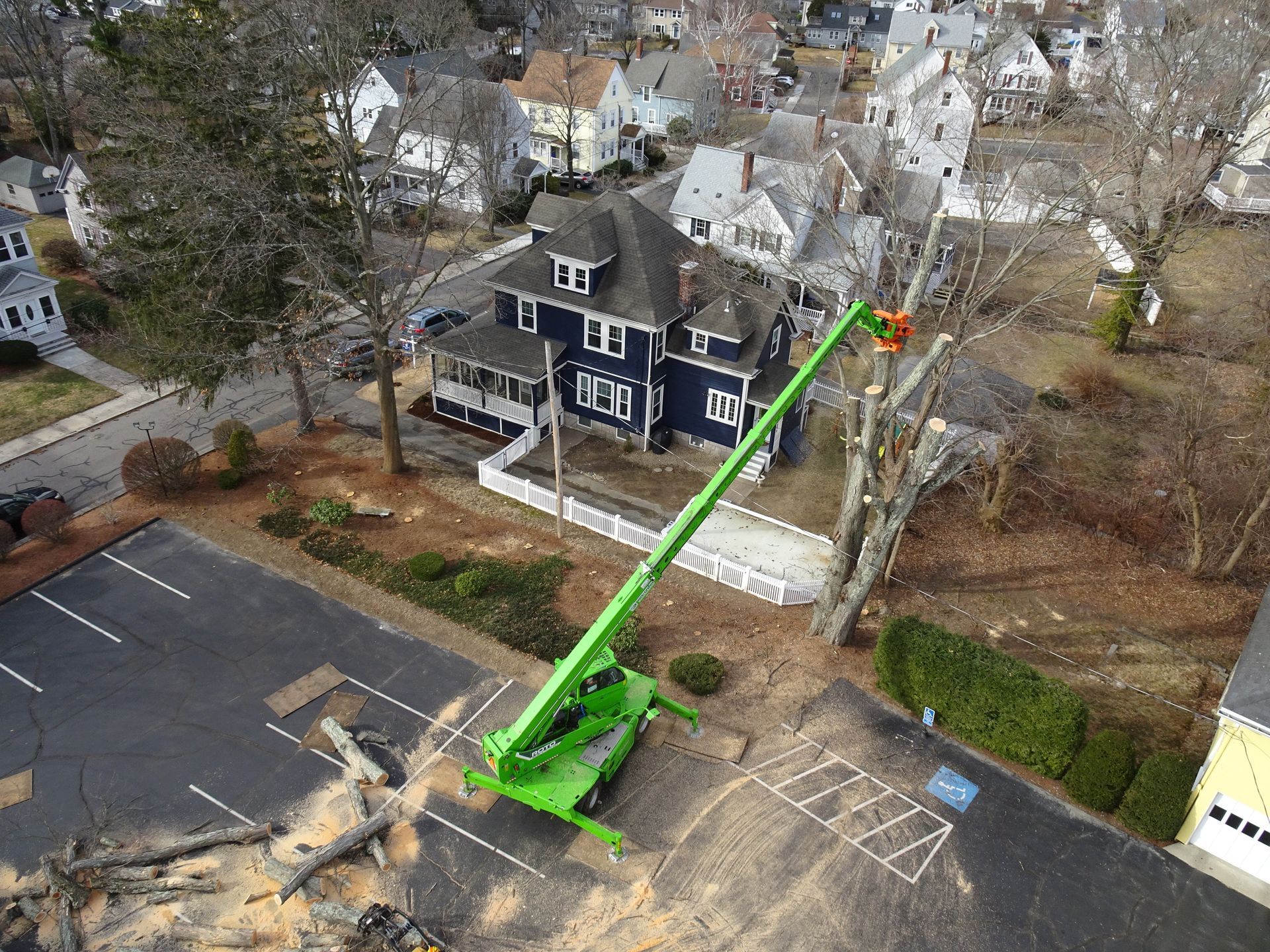 An aerial view of a crane cutting a tree in a parking lot.