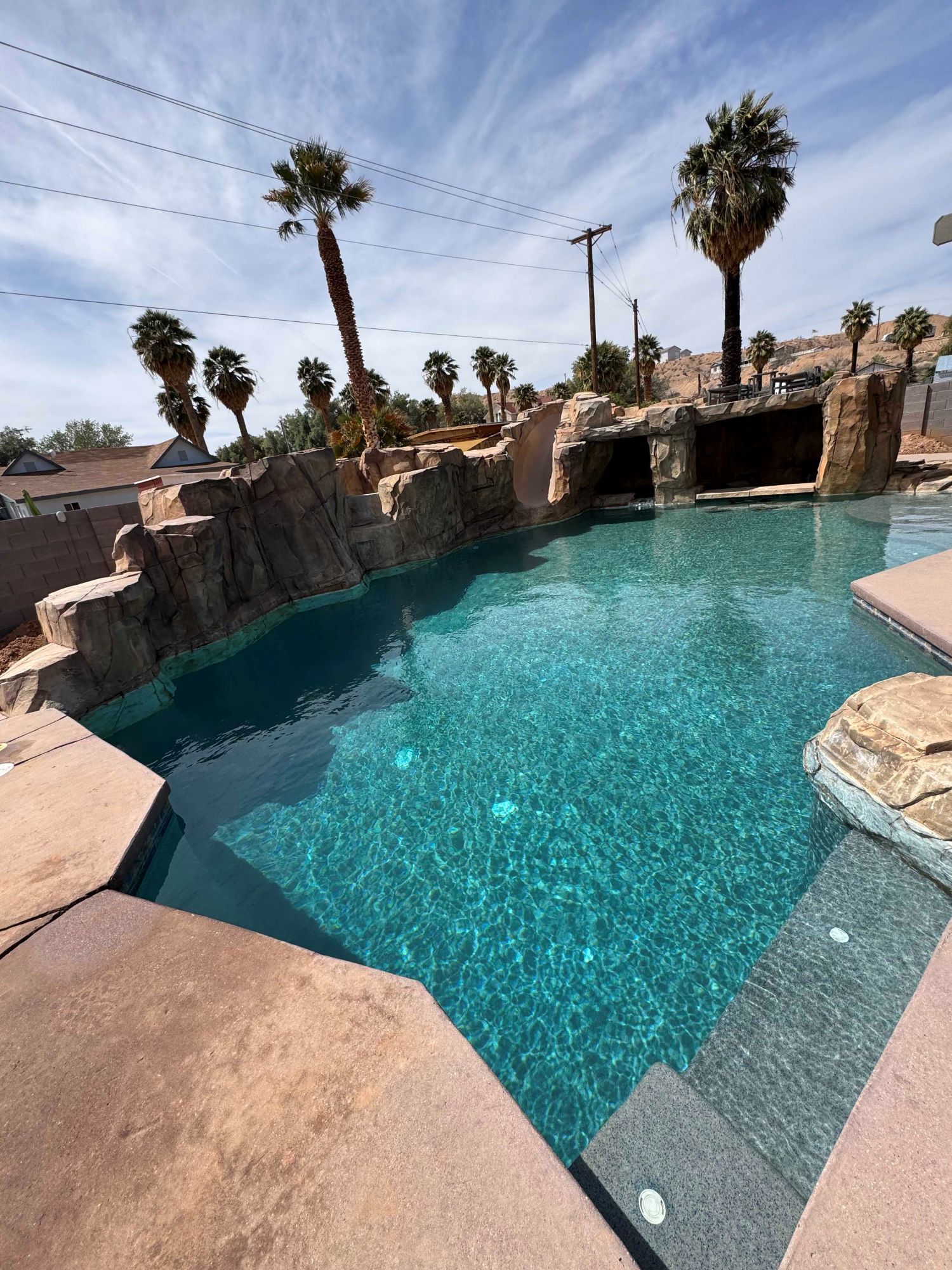 A large swimming pool with a waterfall and palm trees in the background.
