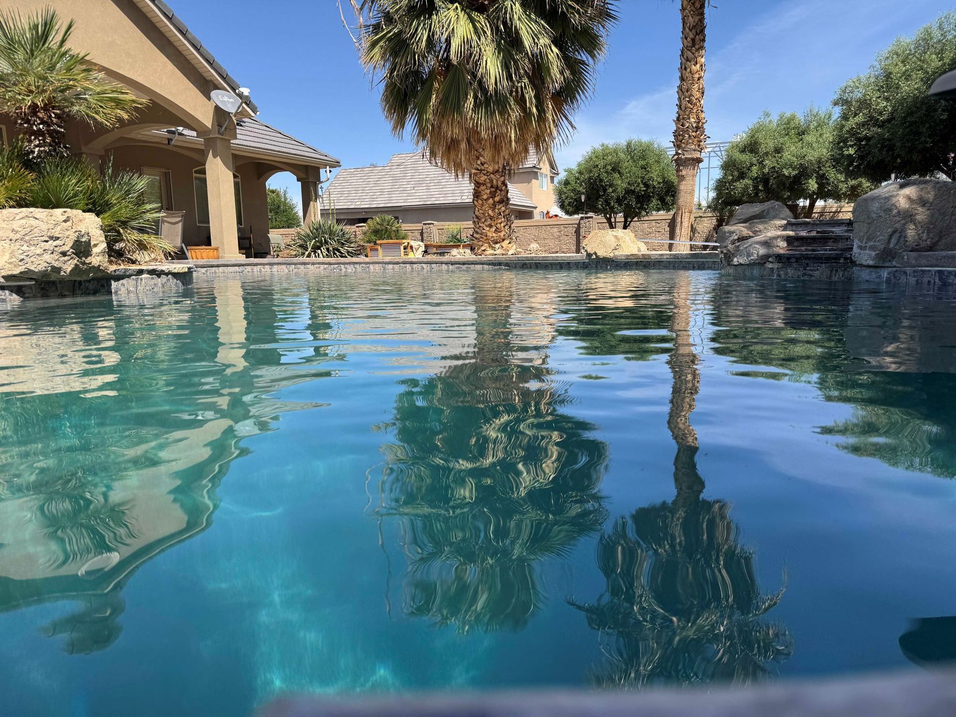 A swimming pool with palm trees in the background and a house in the background.