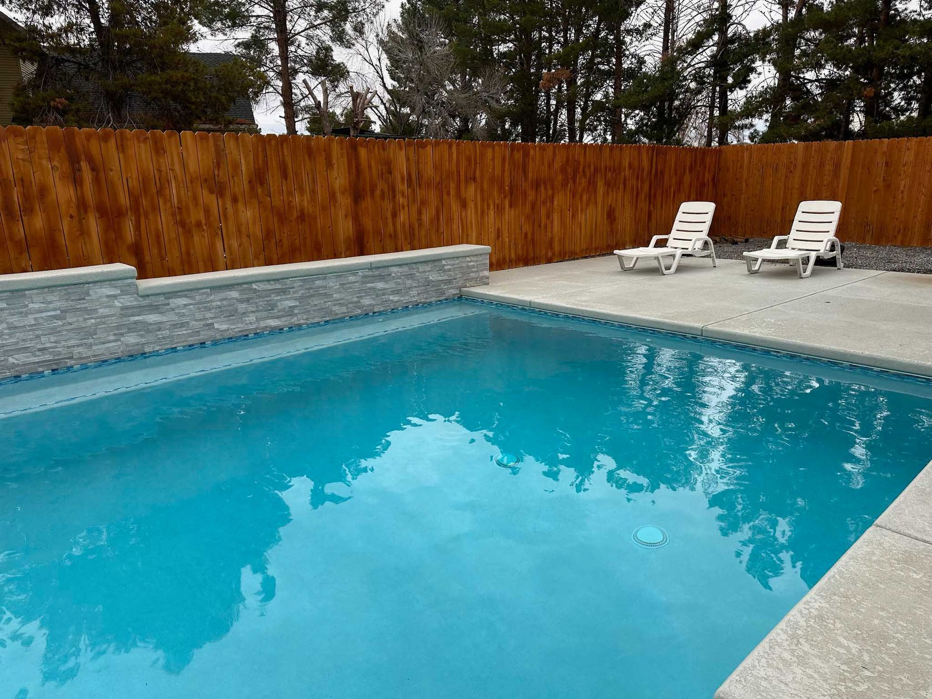 A swimming pool surrounded by chairs and a wooden fence