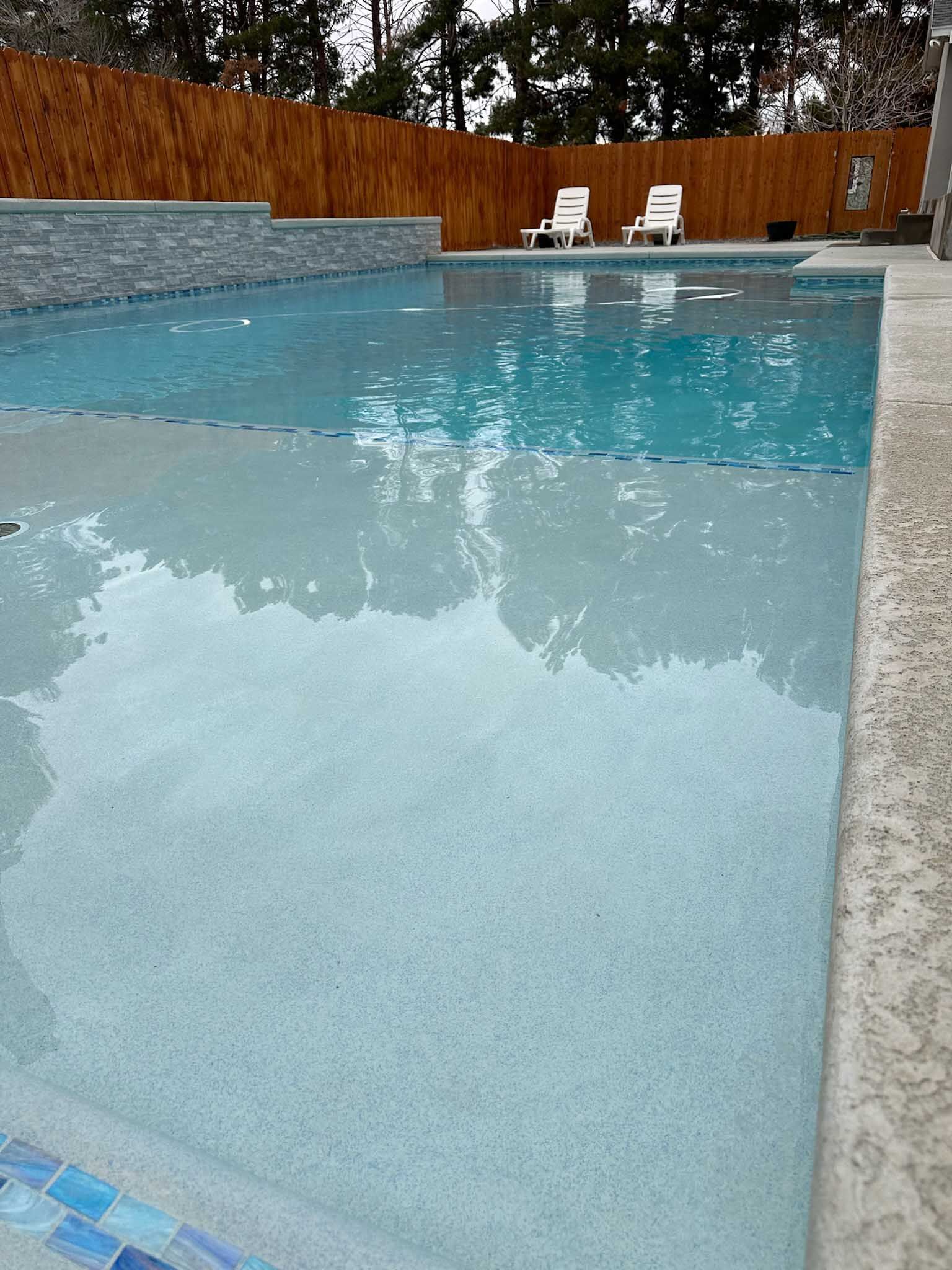 A large swimming pool with a wooden fence and chairs in the background.