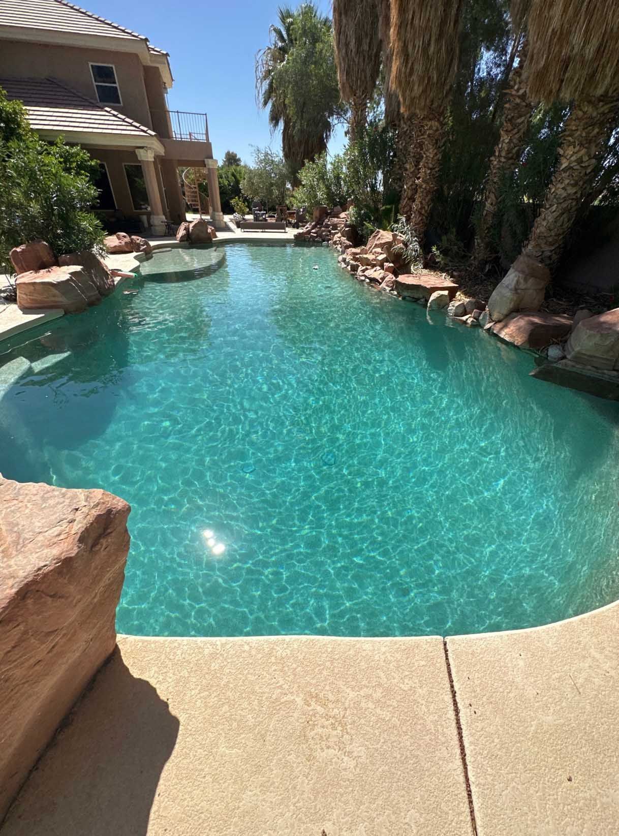 A large swimming pool surrounded by rocks and palm trees in front of a house.