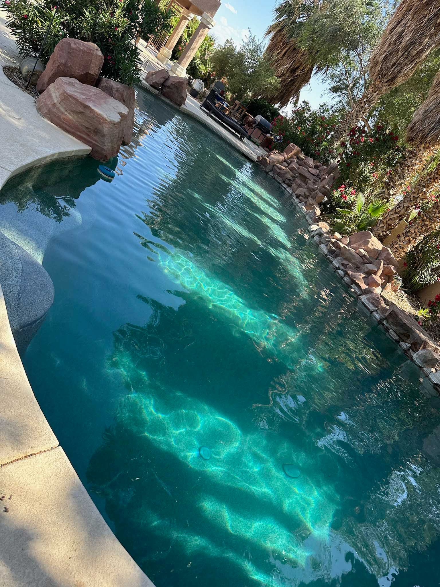 A large swimming pool surrounded by rocks and trees in a backyard.