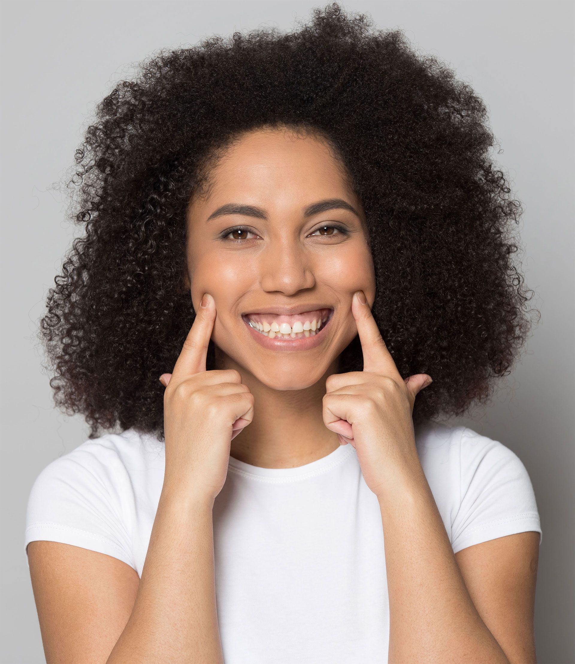 A woman with curly hair is smiling and touching her face with her fingers