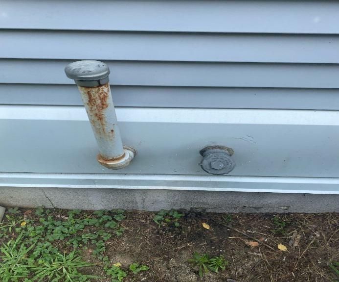 Rusty metal vent pipe and a cap on a gray house siding.