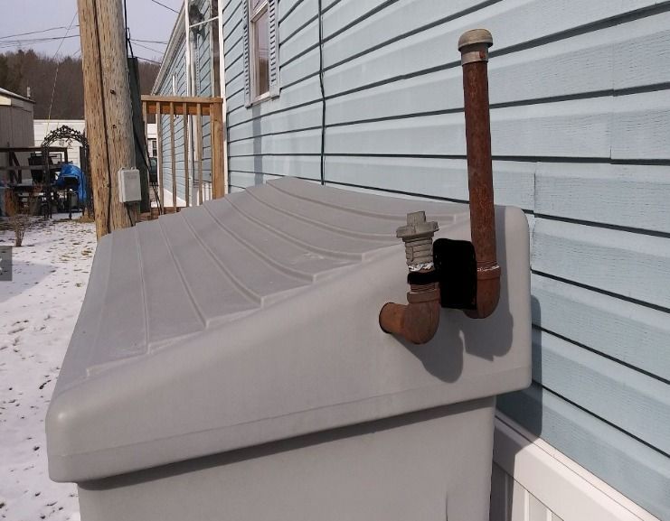 Gray container with a rusty pipe and valve attached to the side of a light blue building.