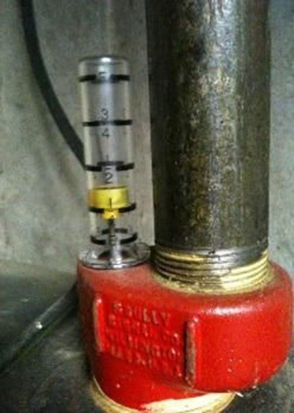 Oil tank gauge with yellow float, red fitting, connected to a metal pipe.