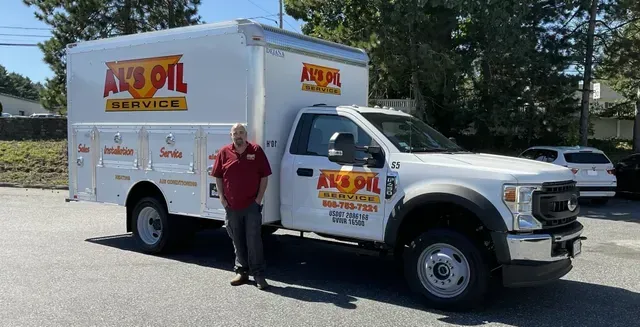 Man in red shirt stands beside a white oil service truck with company logo in outdoor setting.