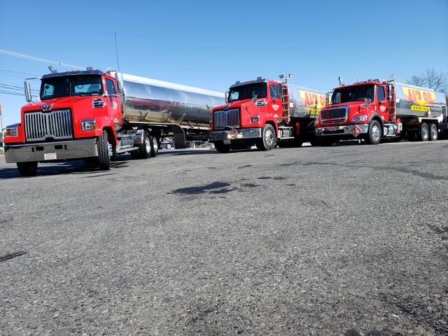 Three red fuel tanker trucks parked on asphalt under a clear blue sky.
