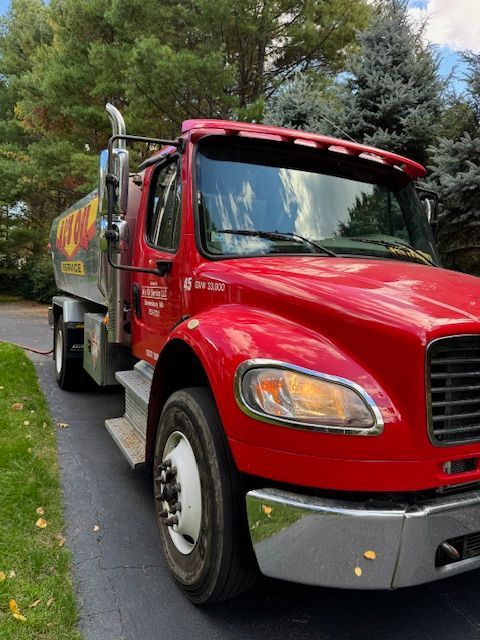 Red oil truck parked on a driveway; a residential setting with trees in the background.