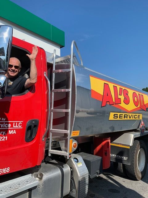 Man waving from a red Al's Oil Service truck with a silver tank, sunny outdoor setting.