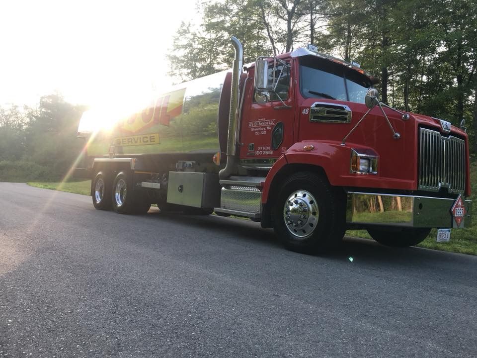 Red tanker truck on a paved road with a bright sun in the background.