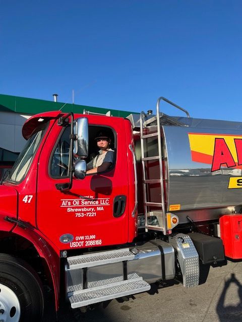 Red oil truck with a driver in the cab, sunny day.