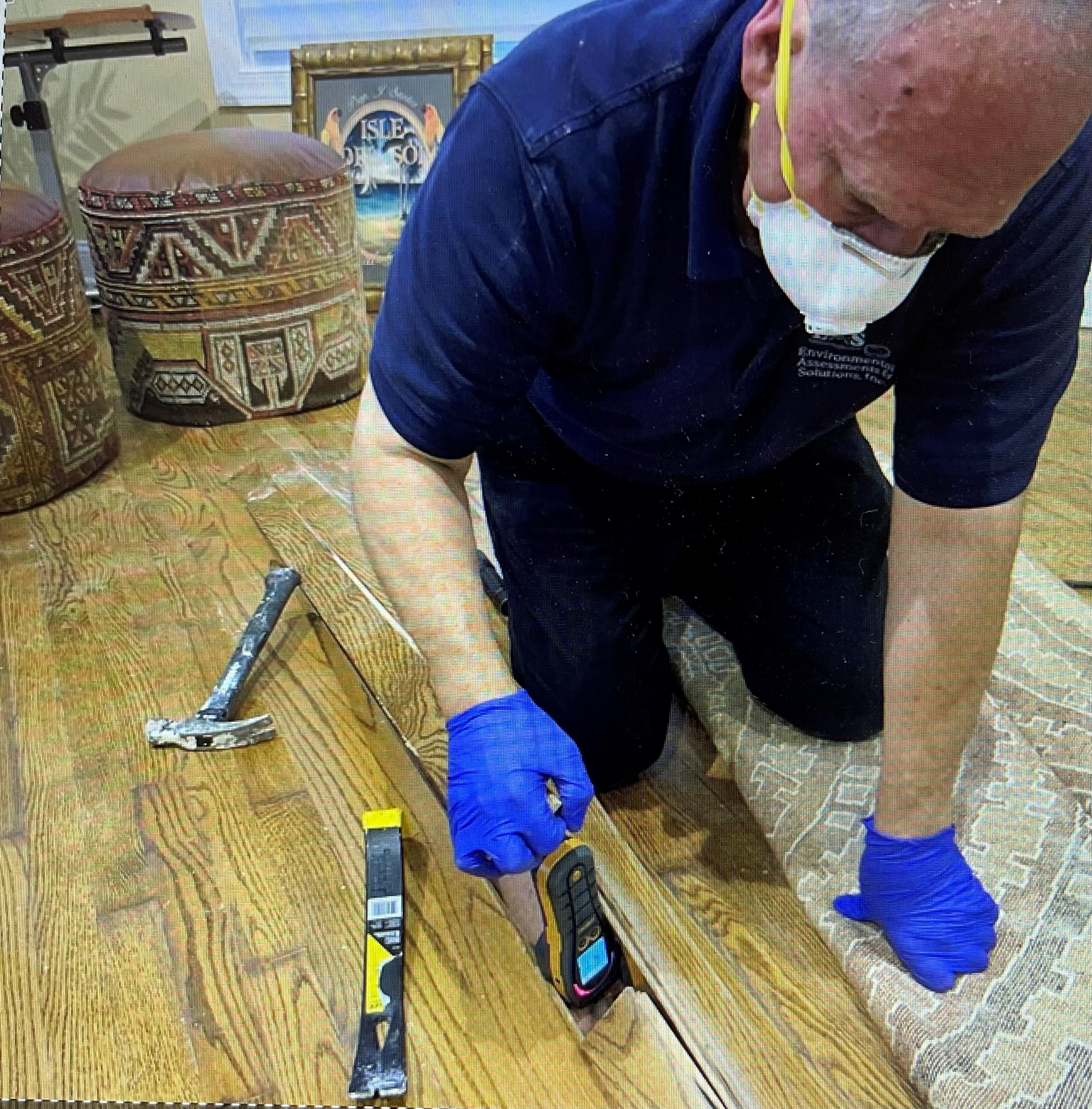 Person kneeling, installing flooring, wearing a mask and gloves. Hammer and tools on wood floor.