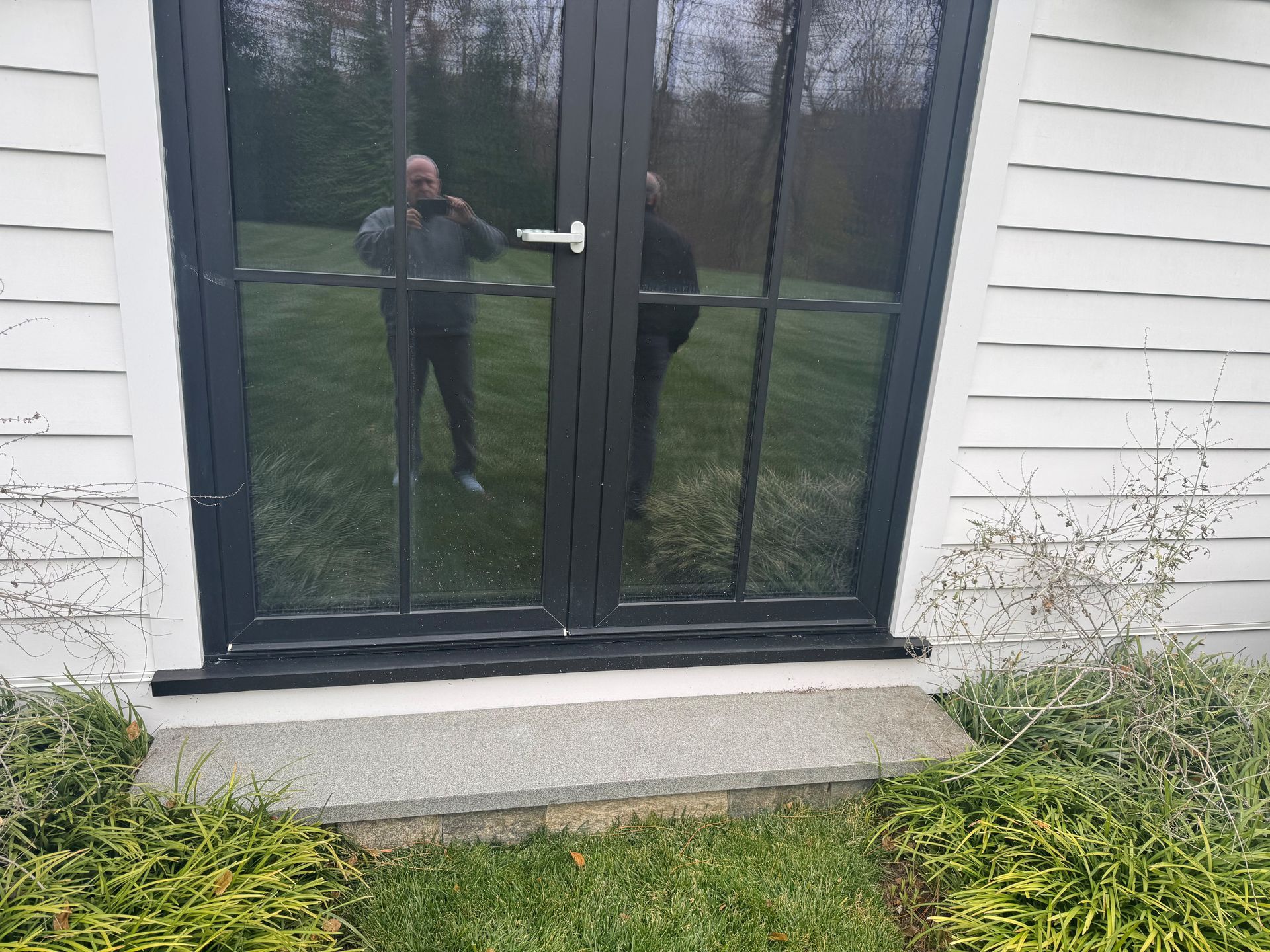 A hand in a glove holds a moisture meter to a damp ceiling near a window frame.