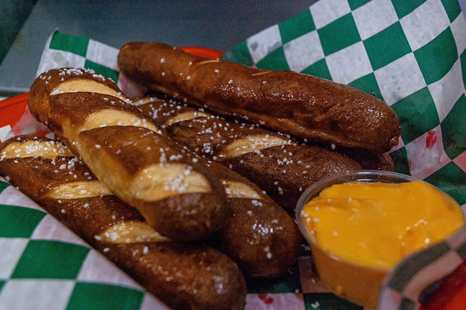 A basket of pretzel sticks with dipping sauce on a checkered paper.