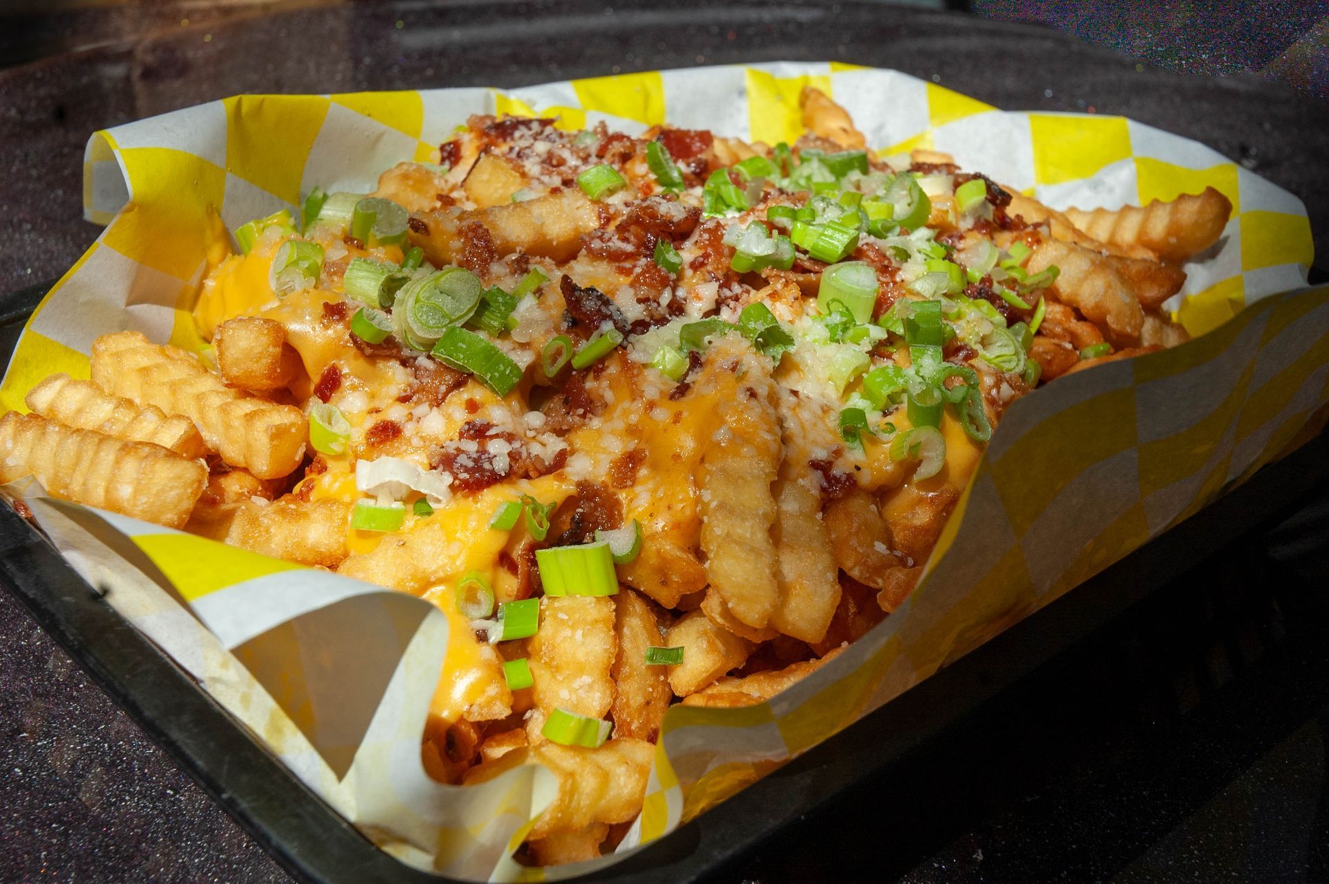 A tray of french fries with cheese , bacon and green onions