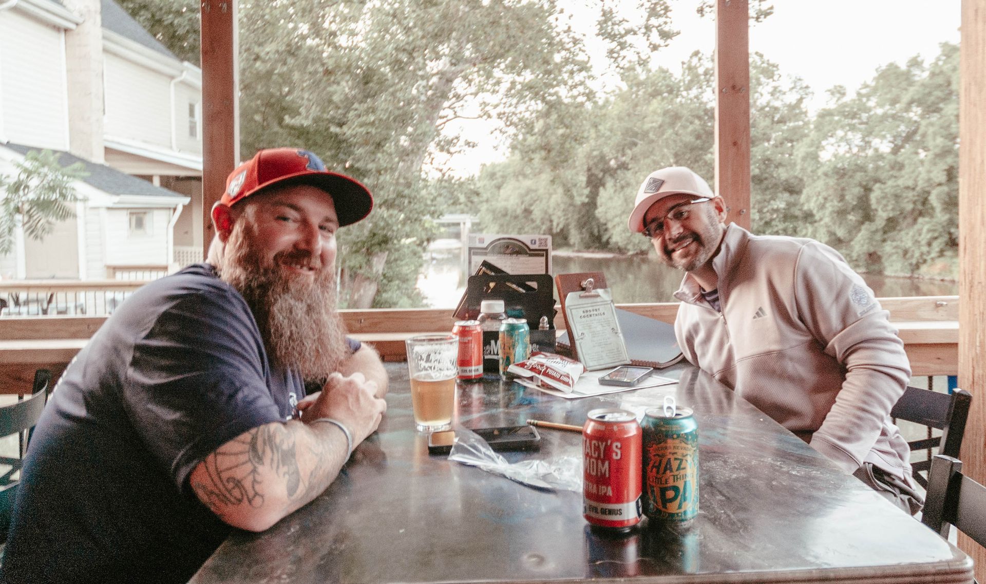 Two men are sitting at a table with cans of beer on it.