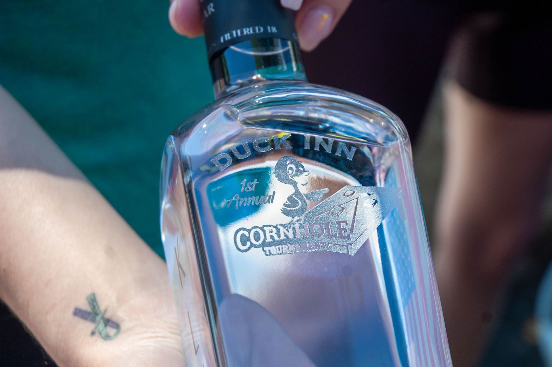 A person with a tattoo on their wrist is holding a bottle of cornish gin.