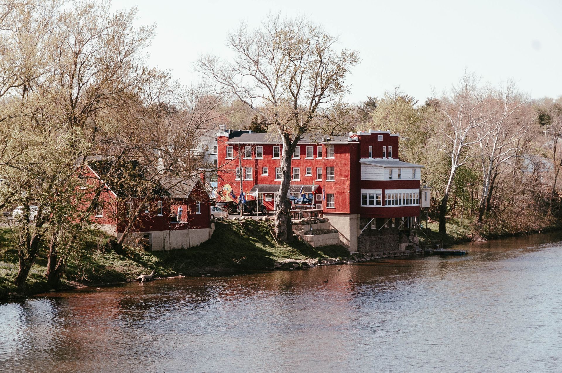 A red building is sitting on the shore of a river surrounded by trees.