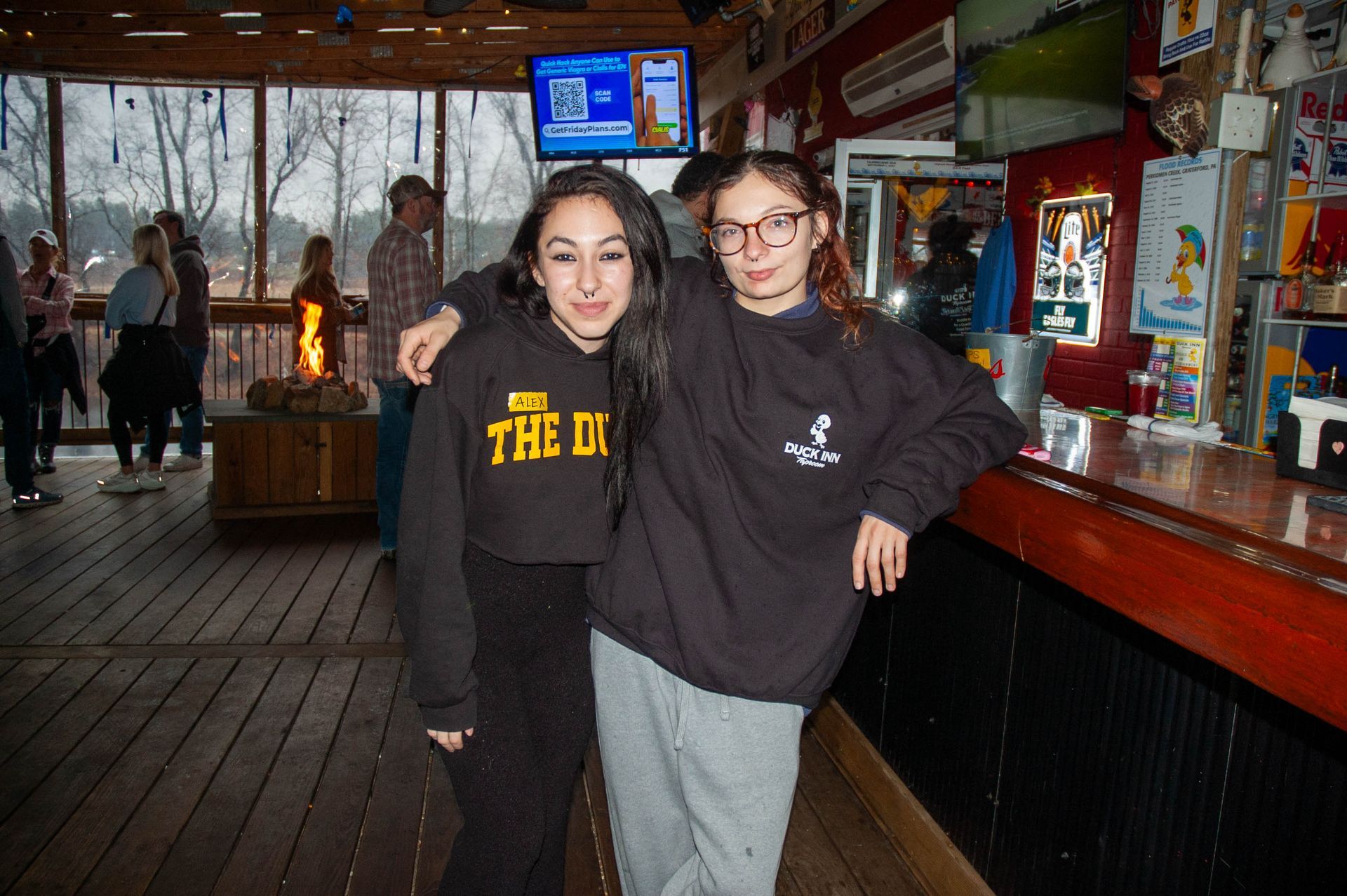 Two girls are posing for a picture in front of a bar.