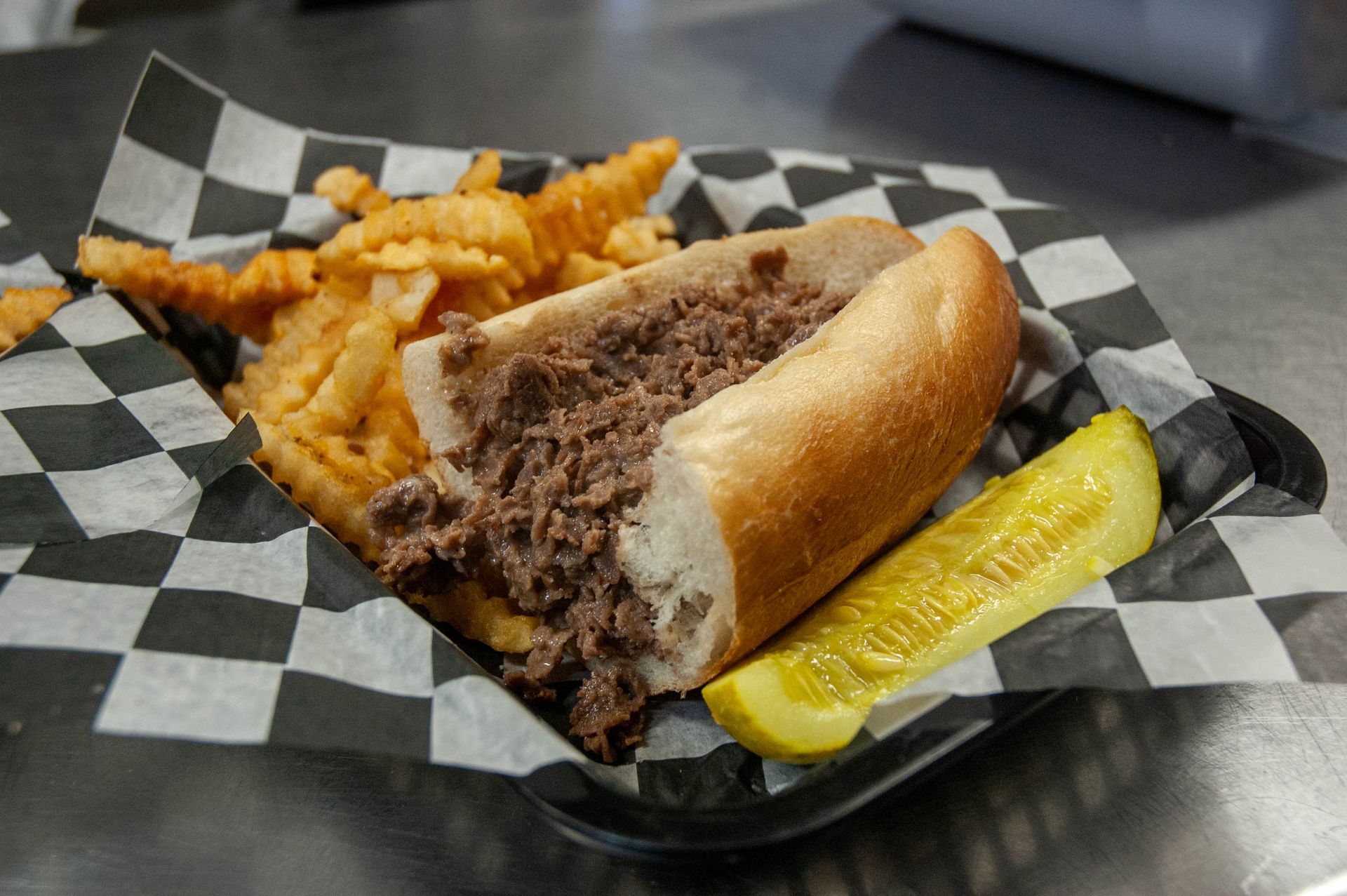 A steak sandwich with french fries and a pickle on a plate.
