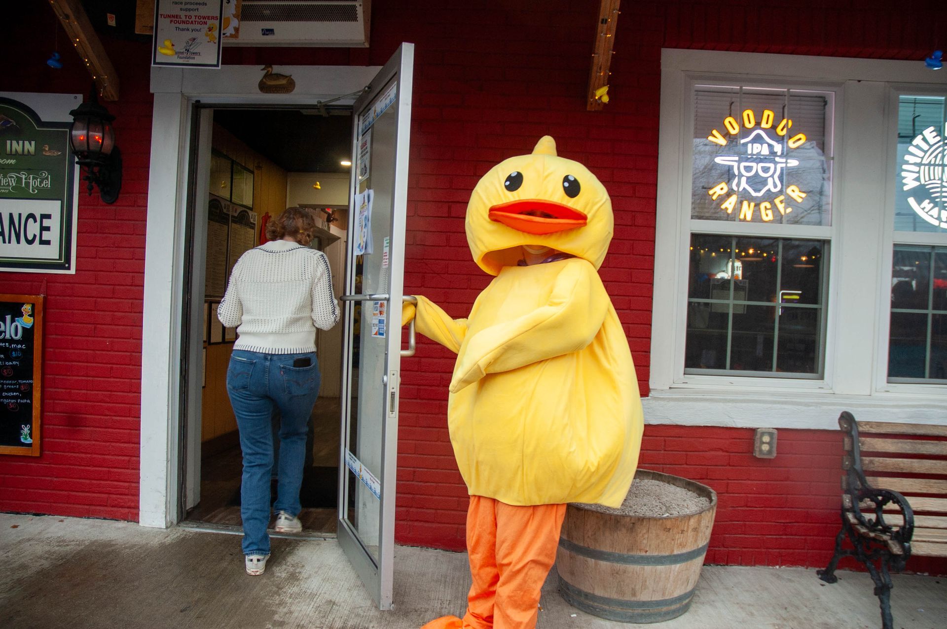 A yellow duck mascot is standing in front of a red building.