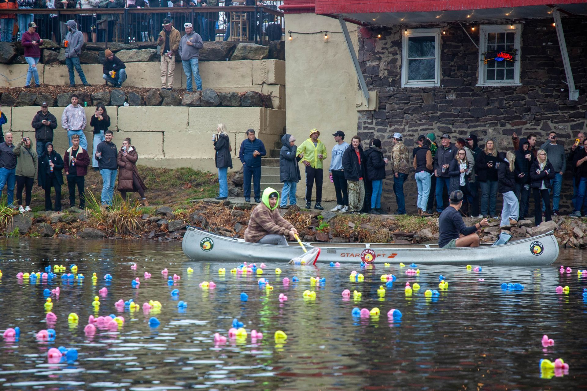 A group of people are watching a man in a canoe in the water.