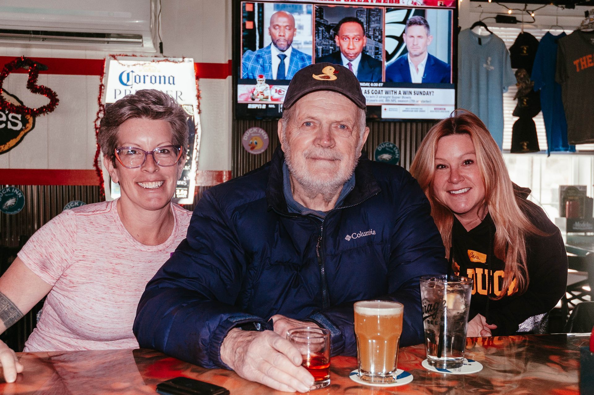 A man and two women are sitting at a bar drinking beer.