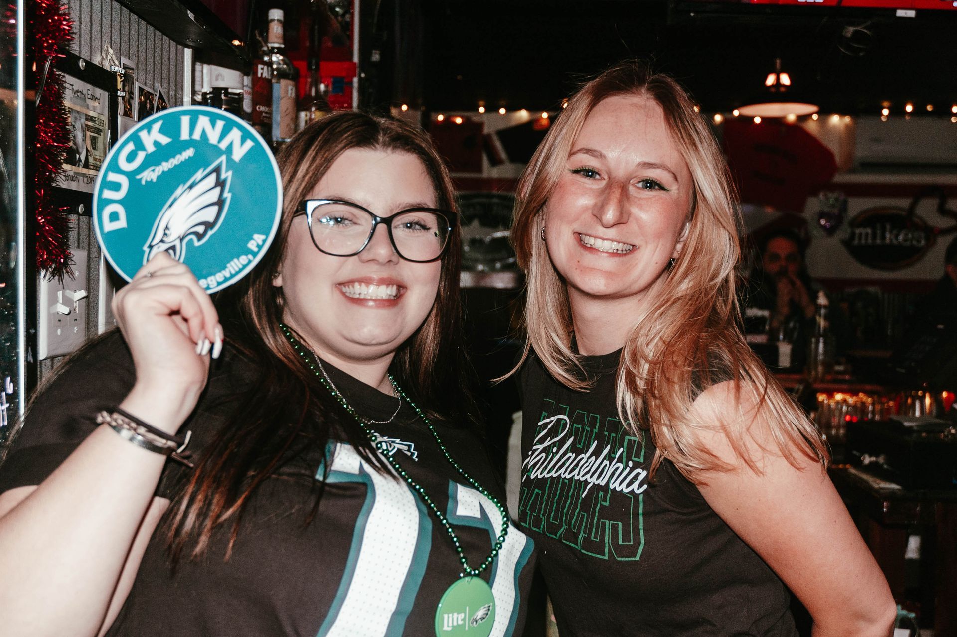 Two women are standing next to each other in a bar holding a sign that says duck inn.