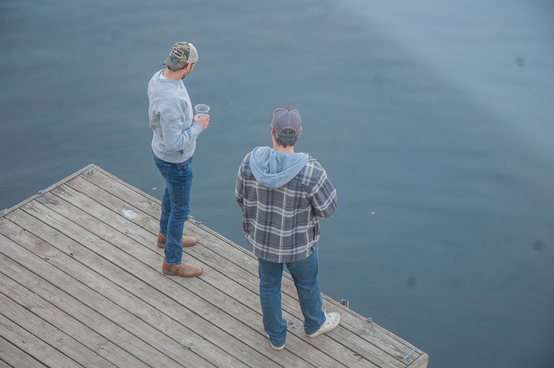 Two men are standing on a dock looking at the water.