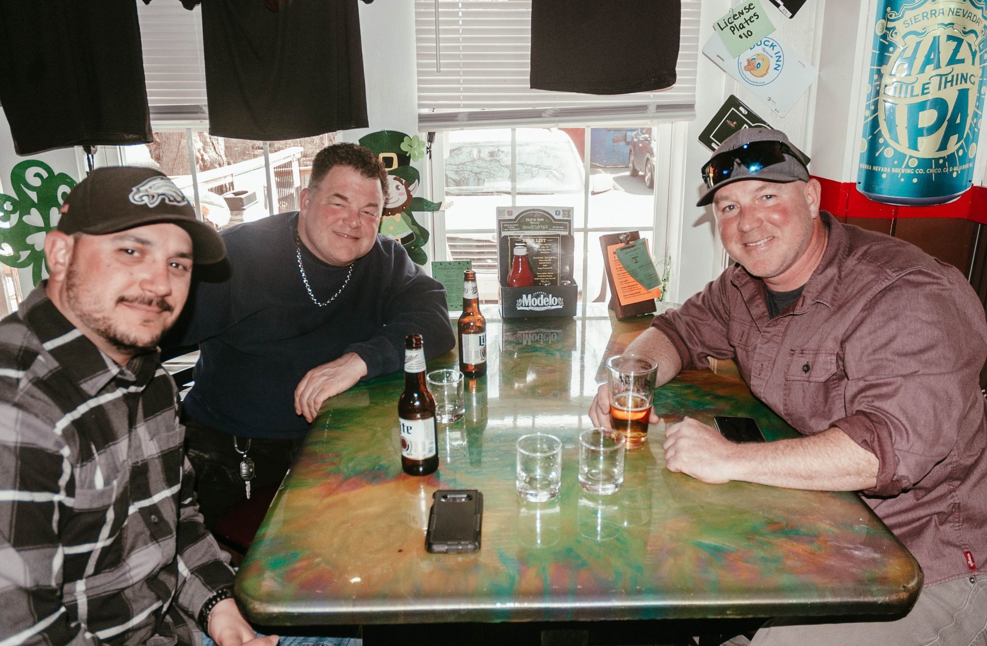 Three men are sitting at a table with bottles of beer.