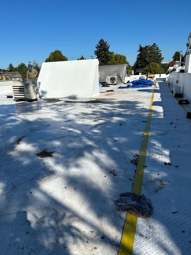 Snow-covered rooftop with a yellow safety line, a large white panel, and scattered equipment under a clear blue sky