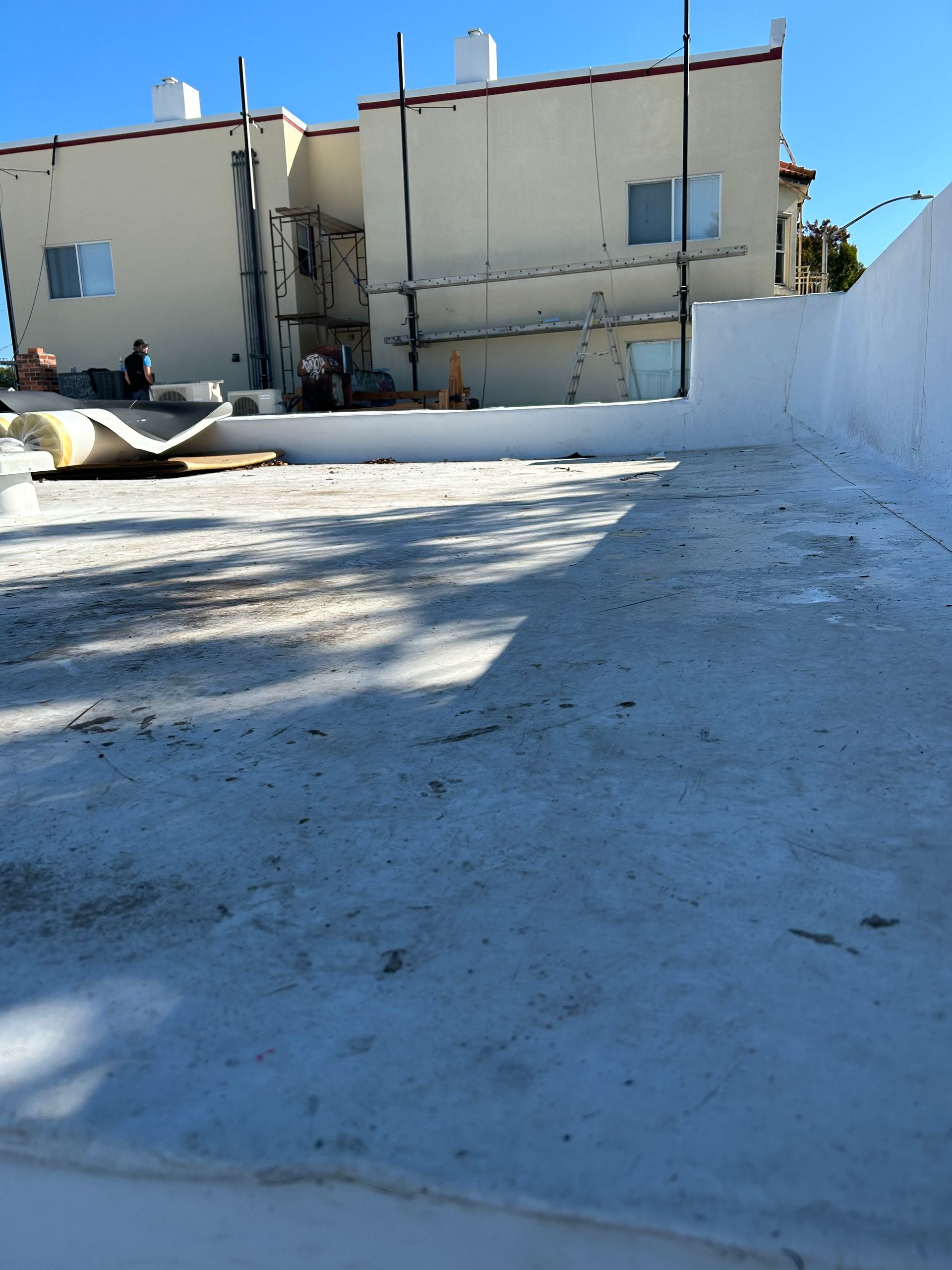 Sunny rooftop courtyard with beige buildings, white walls, and a concrete surface with deep shadows.