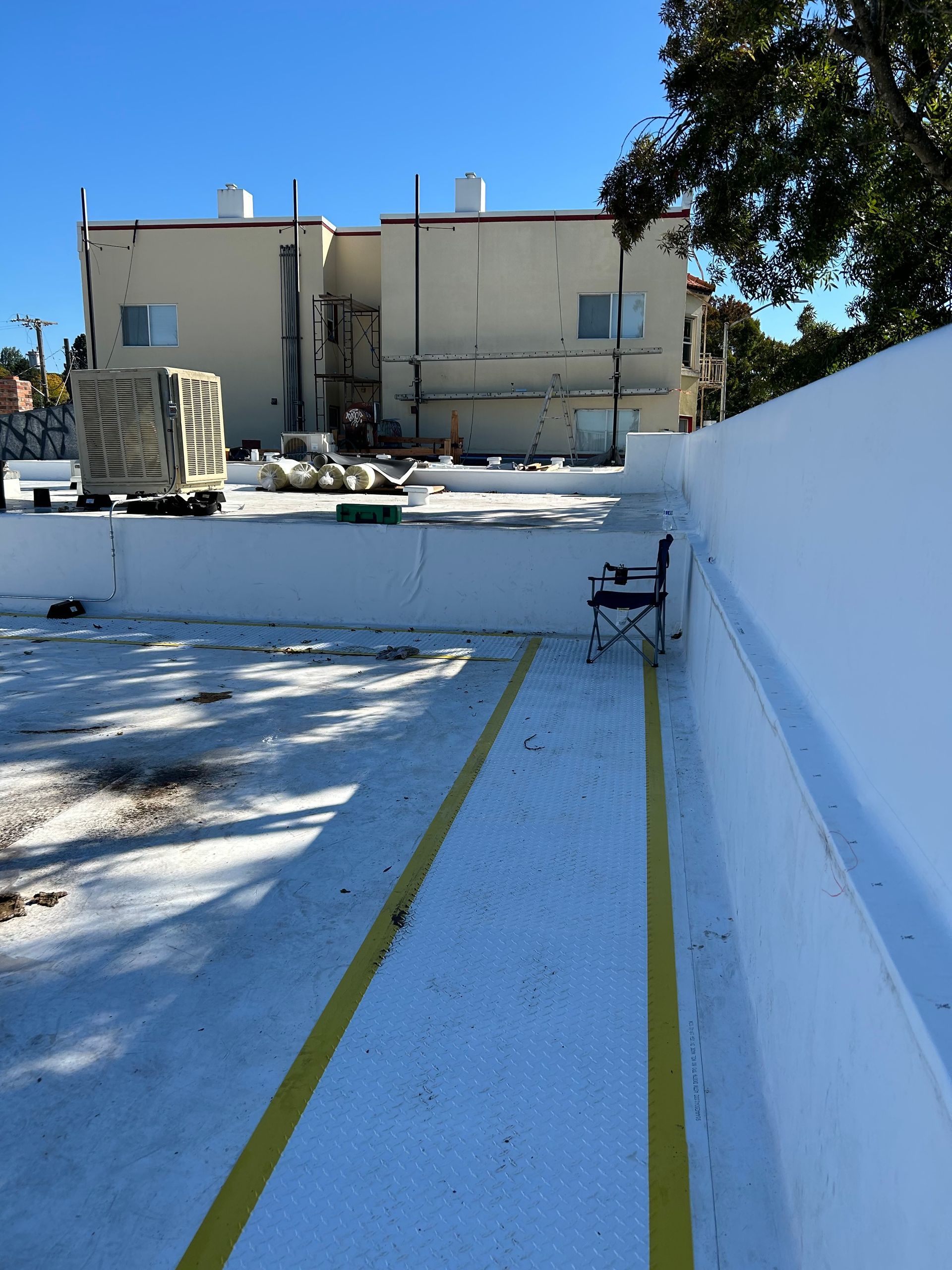 Empty white rooftop with yellow lines and a building in the background, under a blue sky.