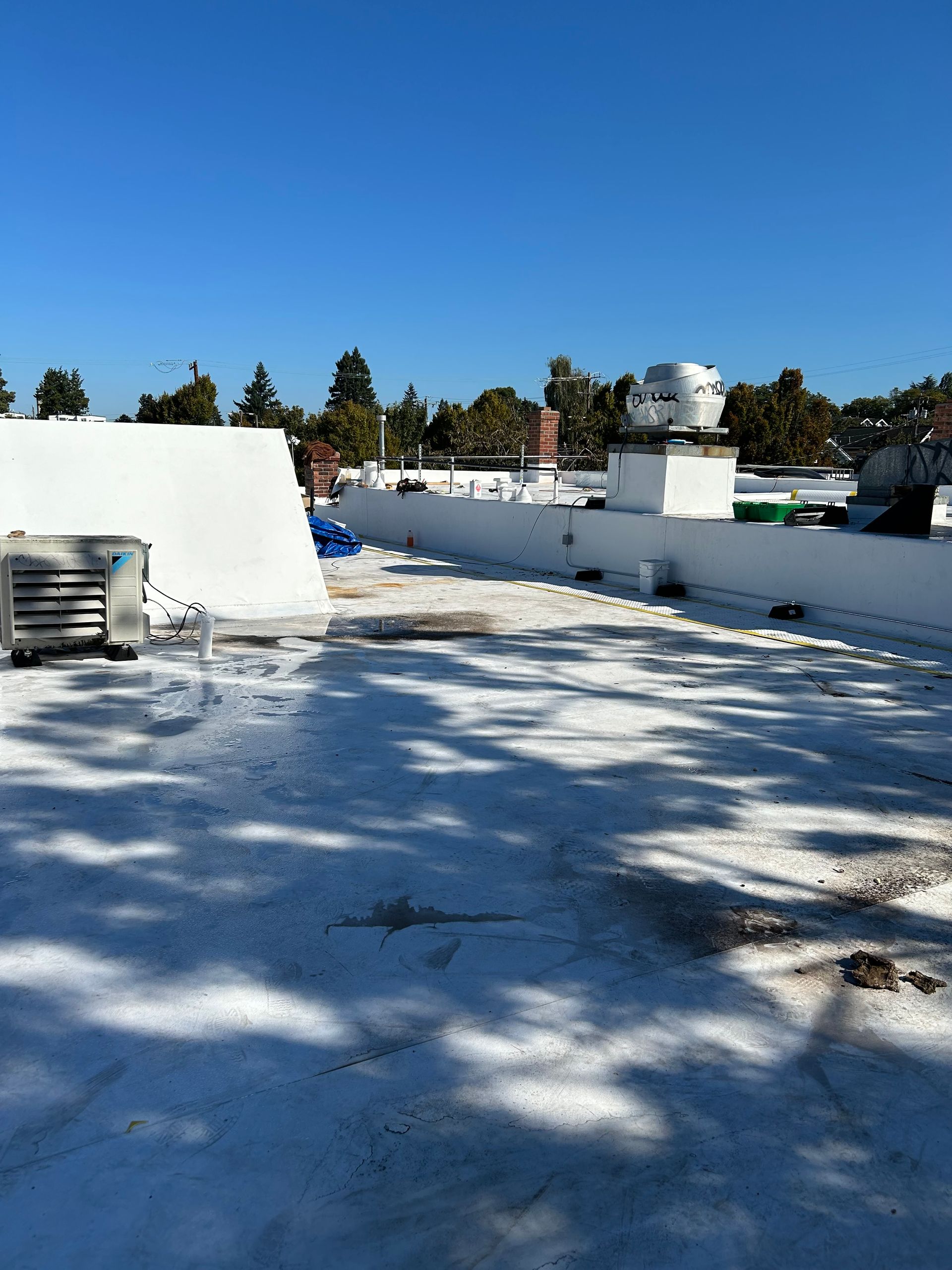 Snow-covered rooftop under a clear blue sky, with white walls and trees in the background.