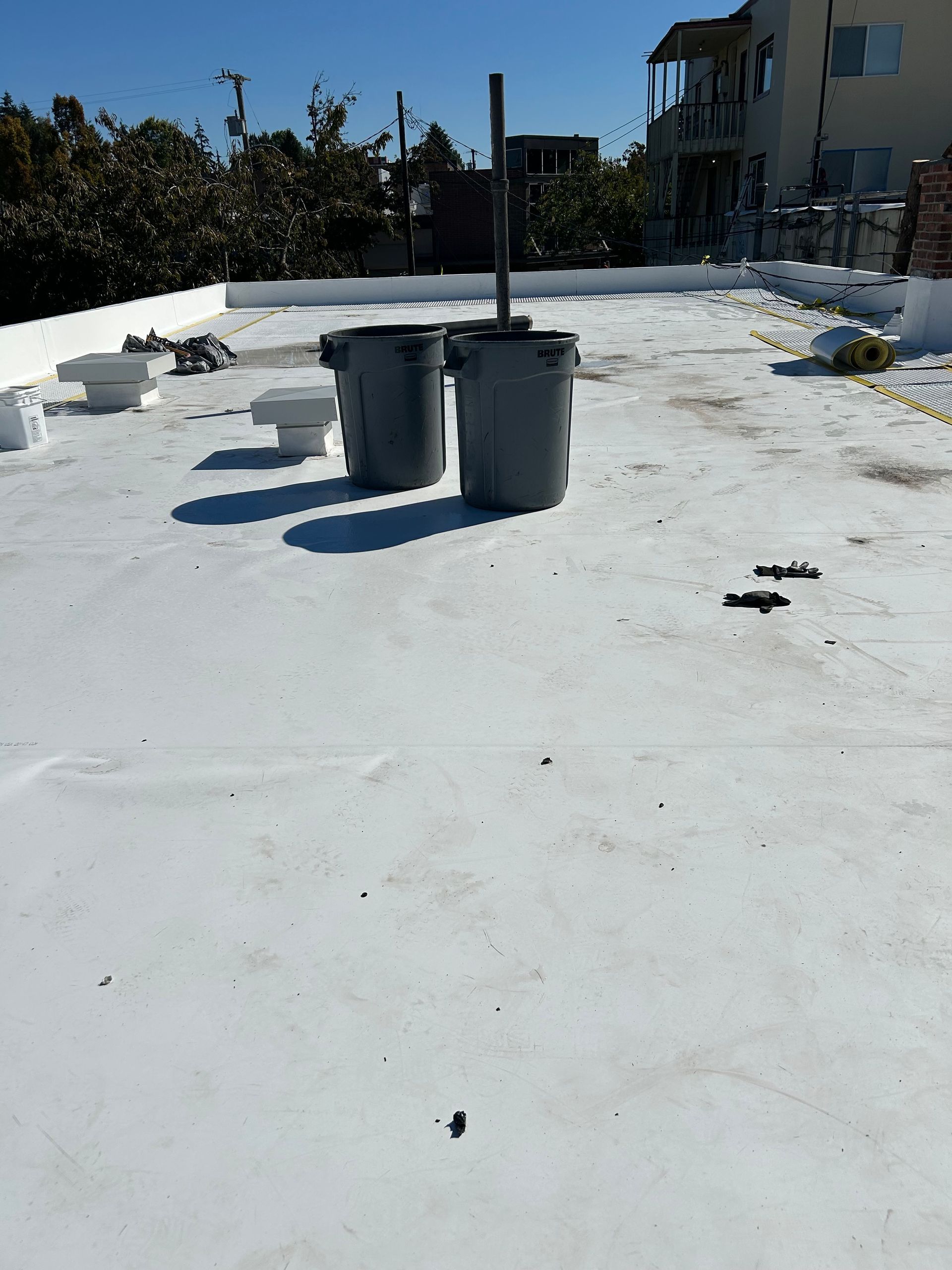 Flat rooftop with gray trash bins and scattered debris under bright sunlight.
