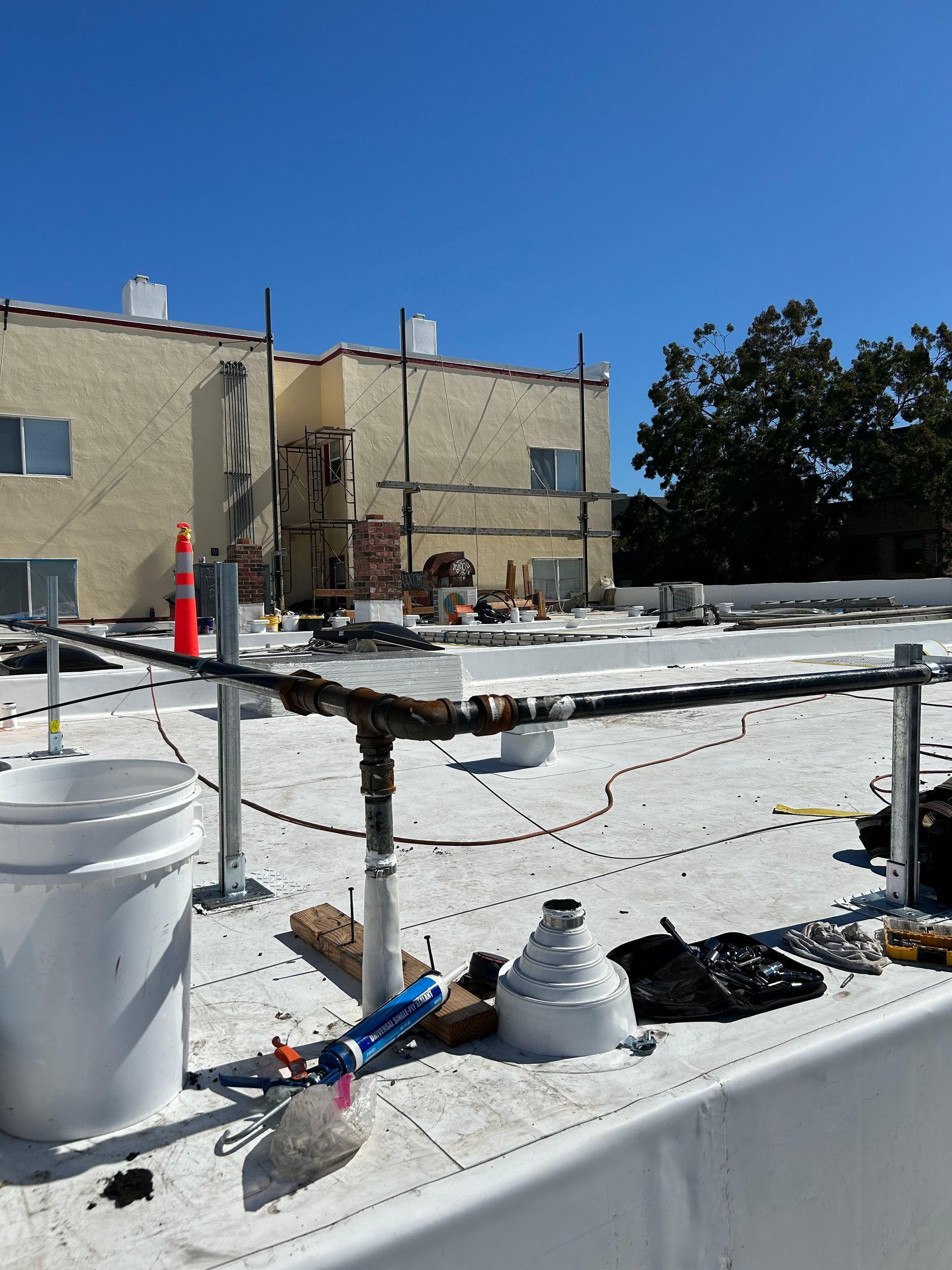 Rooftop under construction with railings, tools, and white coating against a blue sky